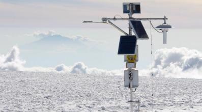 乞力马扎罗山北部冰原海拔5,775米的AWS，带有净辐射计(左侧)和用于温度和湿度传感器的风扇吸气屏蔽(右侧)。背景中有70公里远的梅鲁山。
