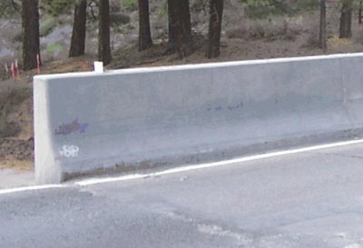A familiar concrete barrier, by the side of the road, made with cement.