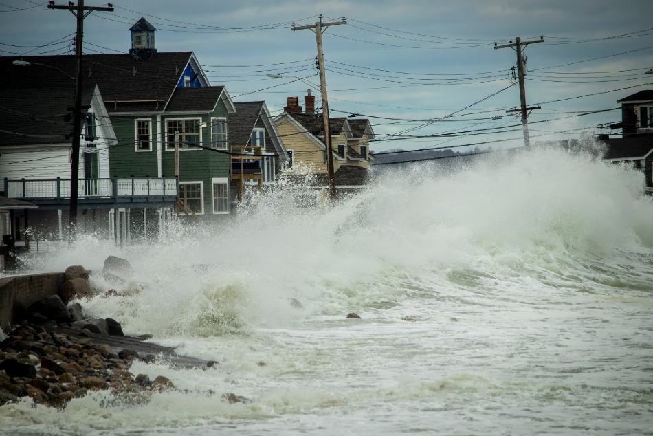 A wave crashing into the shore in front of a row of houses