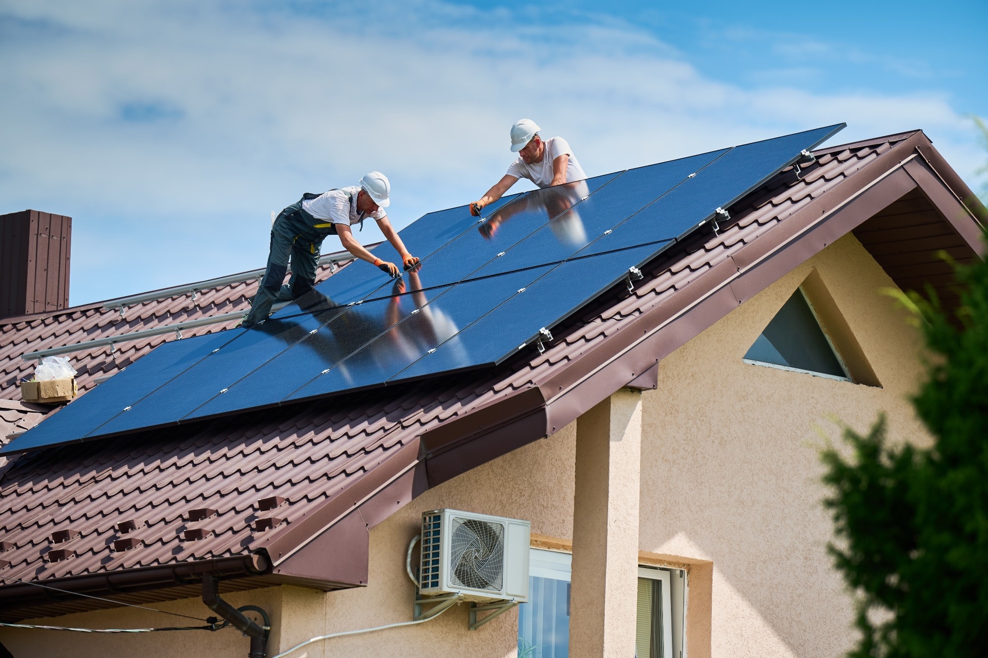 Workers building photovoltaic solar panel system on rooftop of house